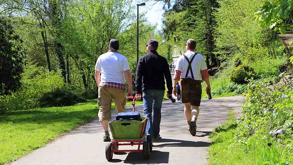 Drei Männer ziehen Bollerwagen durch einen Park