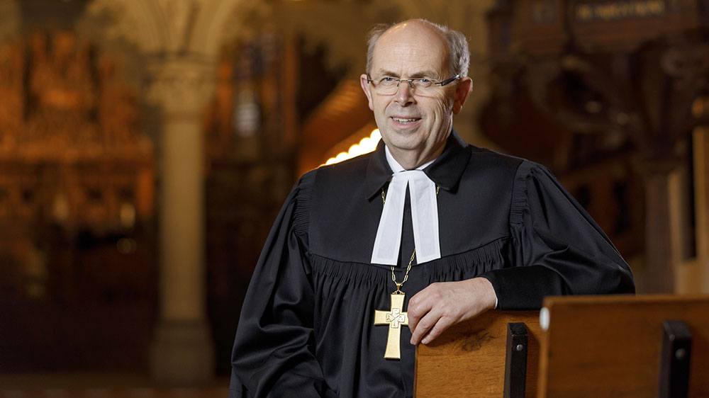 Mann im Talar lehnt an einer Kirchenbank