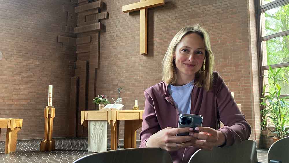 Junge blonde Frau mit ihrem Handy in der Hand in einer Kirche vor dem Altar