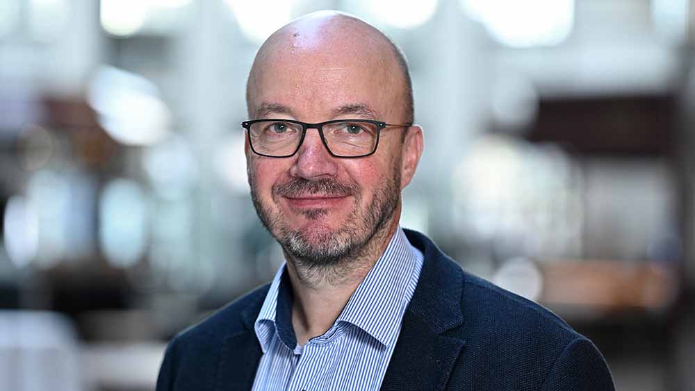 Mann mit Glatze, Bart und Brille im blauen Anzug im Porträt