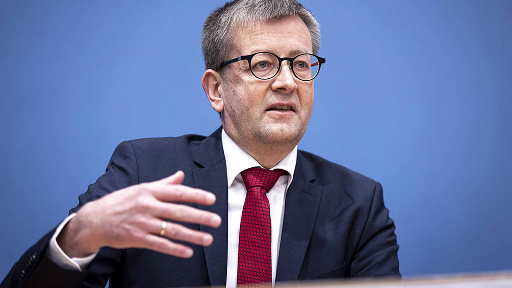 Mann im Anzug sitzt auf Podium und redet