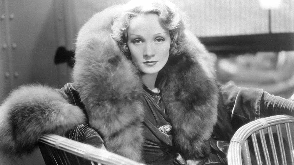 Dietrich im Pelzmantel auf einem Stuhl