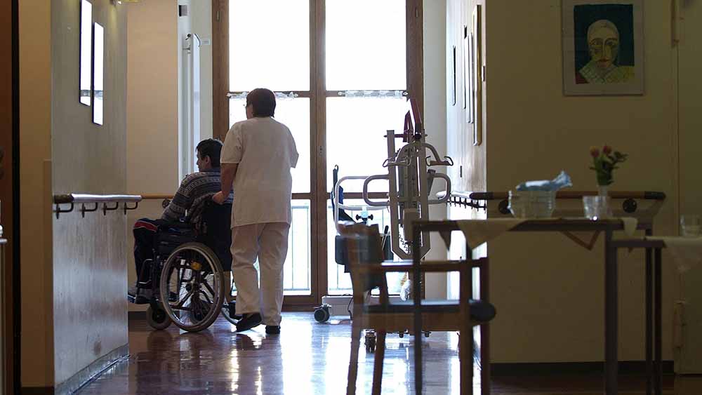 Pflegerin schiebt Person im Rollstuhl über Flur eines Heimes