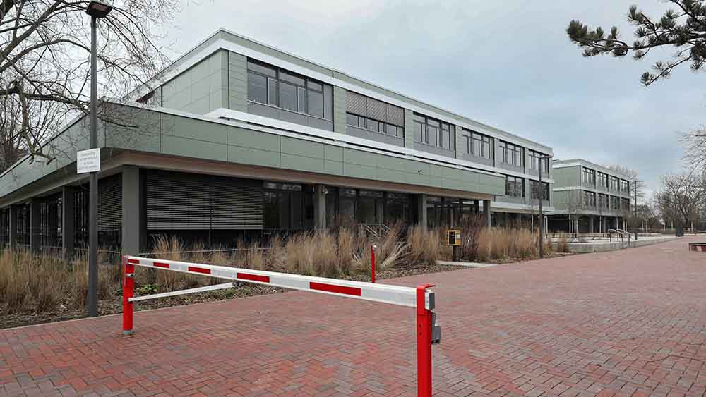 Schulgebäude von Außen fotografiert. Im Vordergrund eine Schranke.