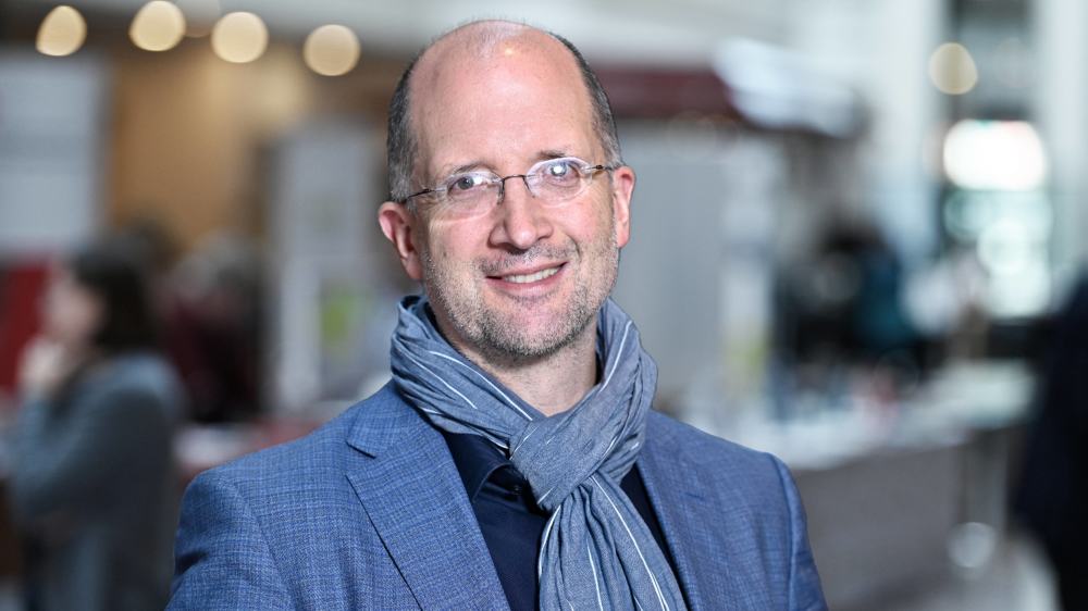 Mann mit Brille, Schal und blauem Anzug lächelt in die kamera