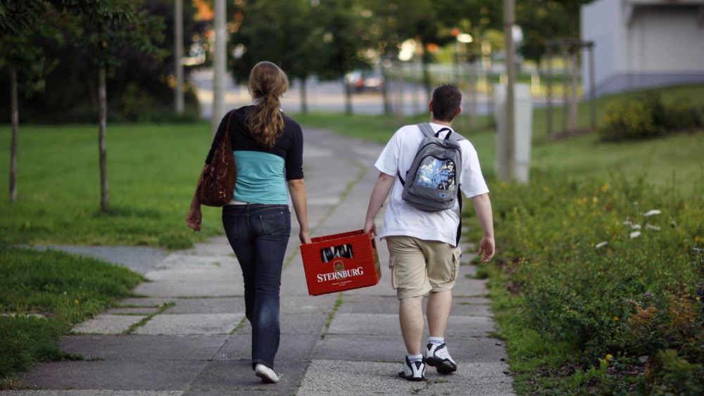 2 Jugendliche tragen eine Kasten Bier durch einen Park