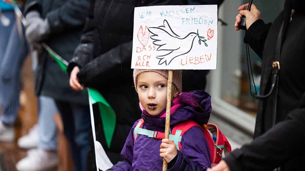 Kind mit verschmiertem Mund in Menschenkette hält Schild mit Friedenstaube hoch