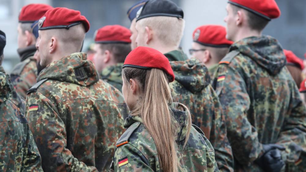 Bundeswehrsoldaten mit roten Mützen stehen in Reih und Glied, von hinten fotografiert.