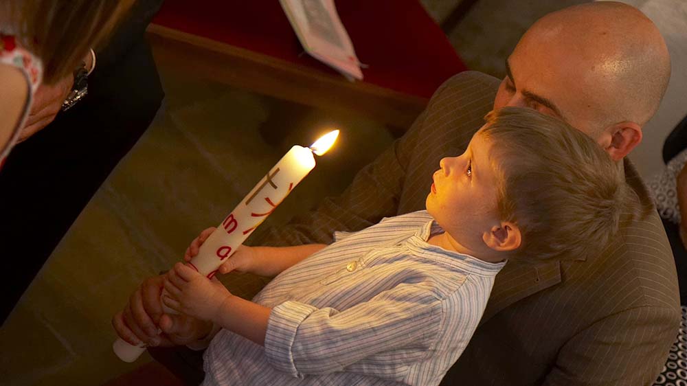 Kleiner Junge hält eine große brennende Kerze. Mann steht hinter ihm