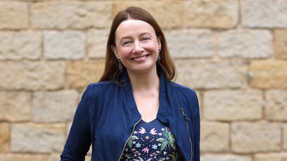 Julia Glombiewski in einer blauen Jacke vor einem Backstein-Hintergrund