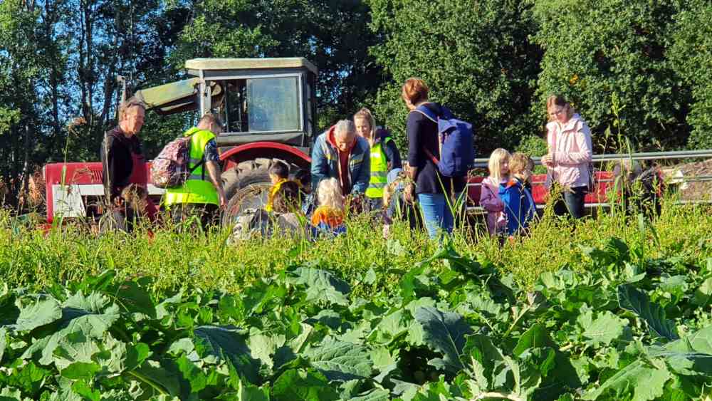 Auf einem Feld steht eine Gruppe Kinder und Erwachsene neben einem Trektor.