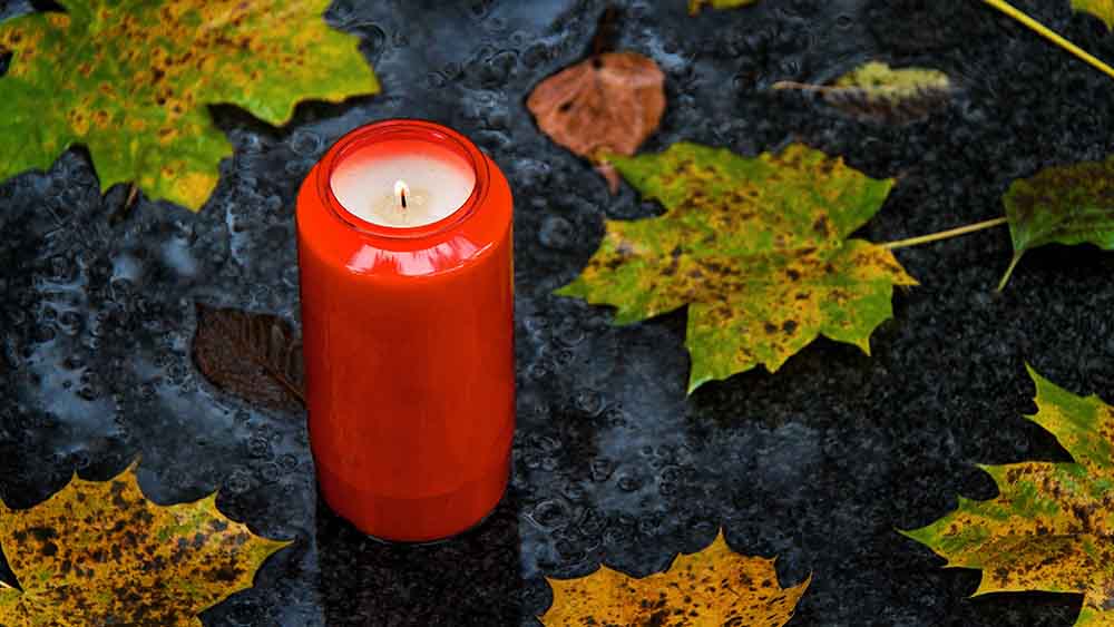 Rote Kerze brennt, drum herum liegen Blätter