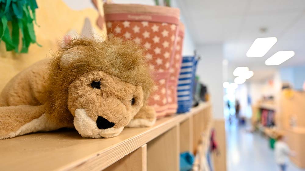 Auf einem Regal in einer Kita liegen ein Kuscheltier und eine Tasche