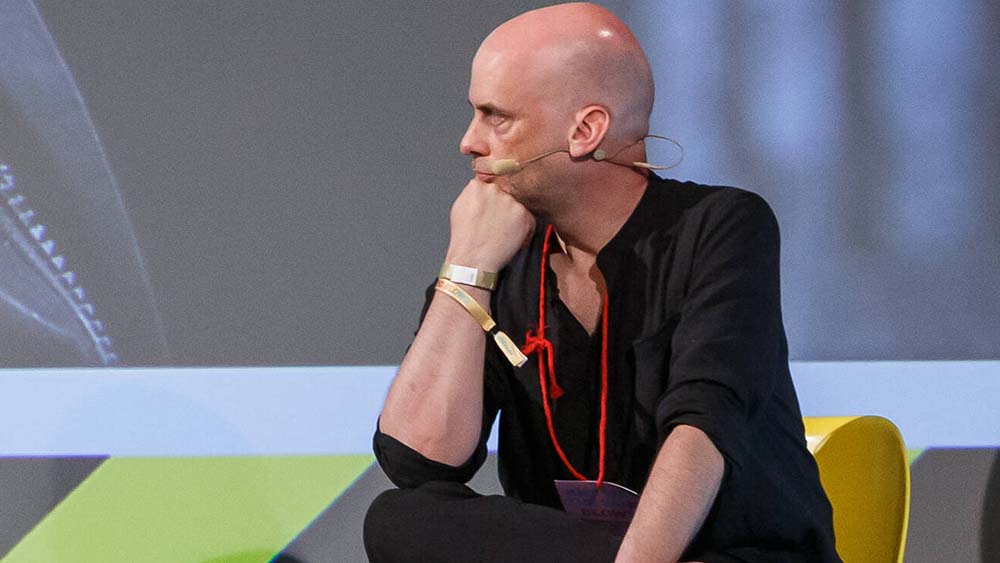 Mann mit Glatze sitzt auf einem Podium und schaut zur Seite