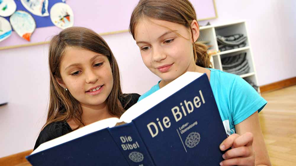 Zwei Mädchen blättern in einer blauen Bibel