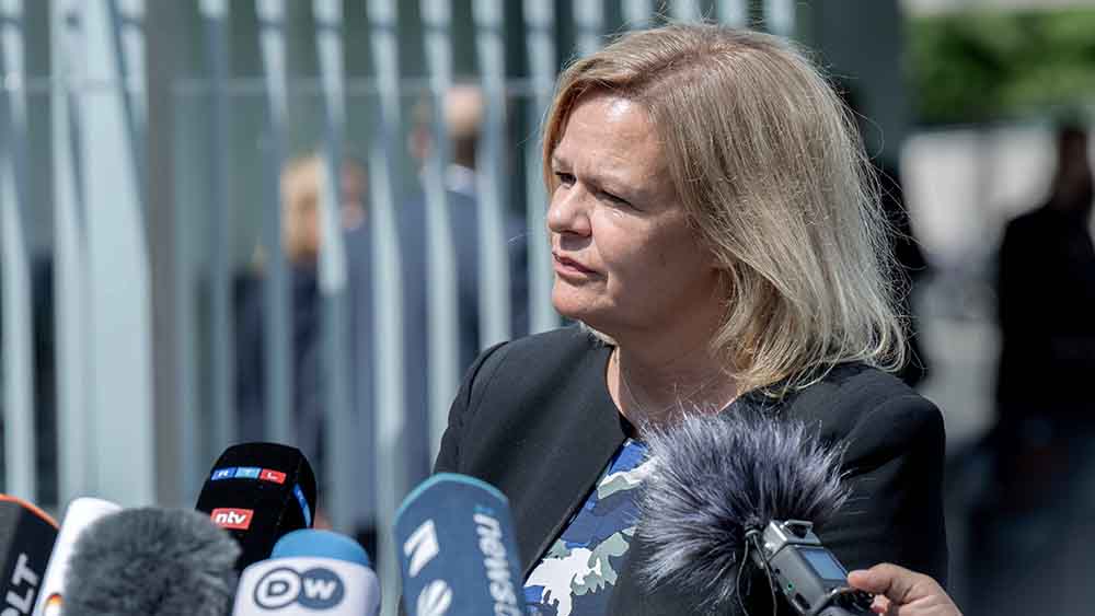 Blonde Frau im schwarzem Blazer steht unter freiem Himmel vor mehreren Mikrofonen