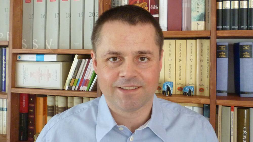 Porträt: Mittelalter Mann mit dunklen, kurzen Haaren vor einem Bücherregal