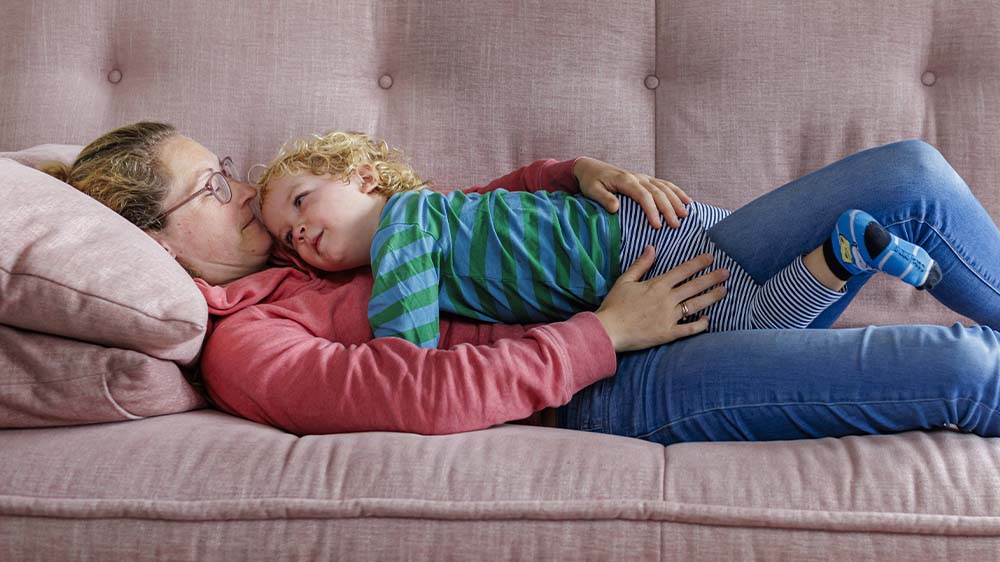 Mutter liegt auf dem Sofa mit Kleinkind auf dem Bauch