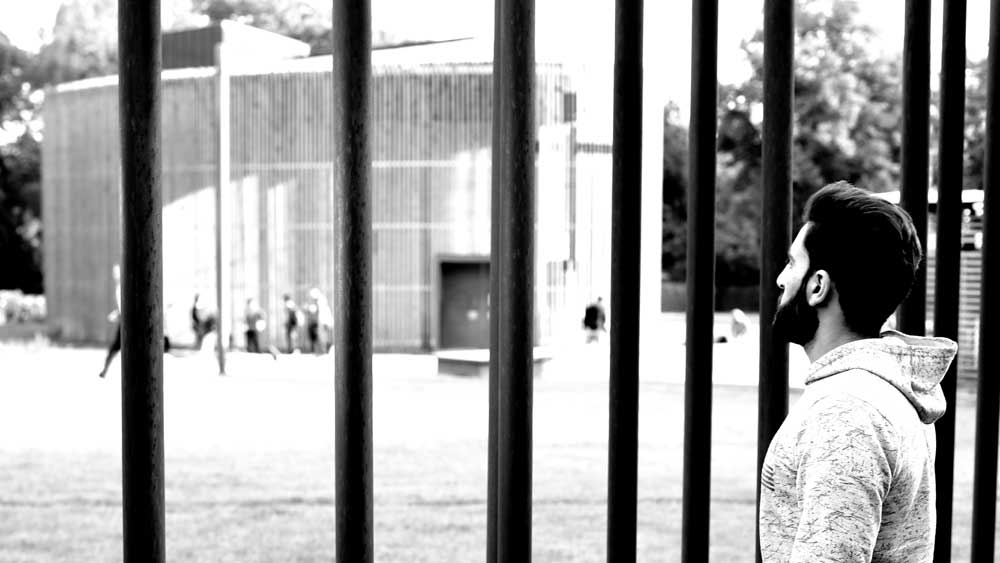 Geflüchteter schaut durch die Metallstäbe zur Kapelle der Versöhnung