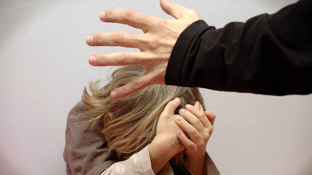 Blondes Mädchen hält sich die Hände schützend vors Gesicht, während eine Männerhand nach ihr greift