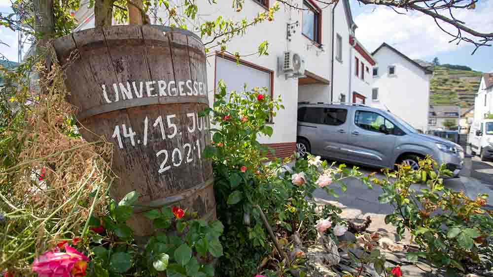 Auf einem Holzstück steht "Unvergessen 14./15. Juli 2021", dahinter ist ein Haus zu sehen