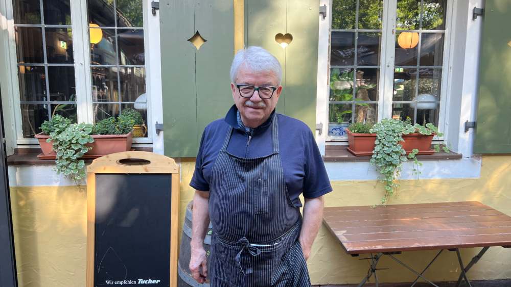 In Mann in Schürze vor einer Gaststätte