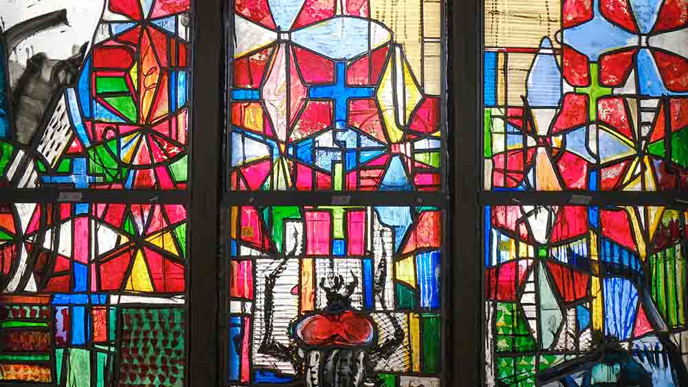 Buntes Kirchenfenster in Nahaufnahme. Aufgemalte Fliege im unteren Drittel