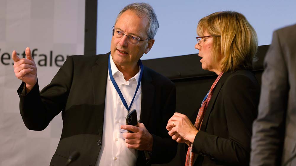 Mann auf einem Podium redet mit einer Frau