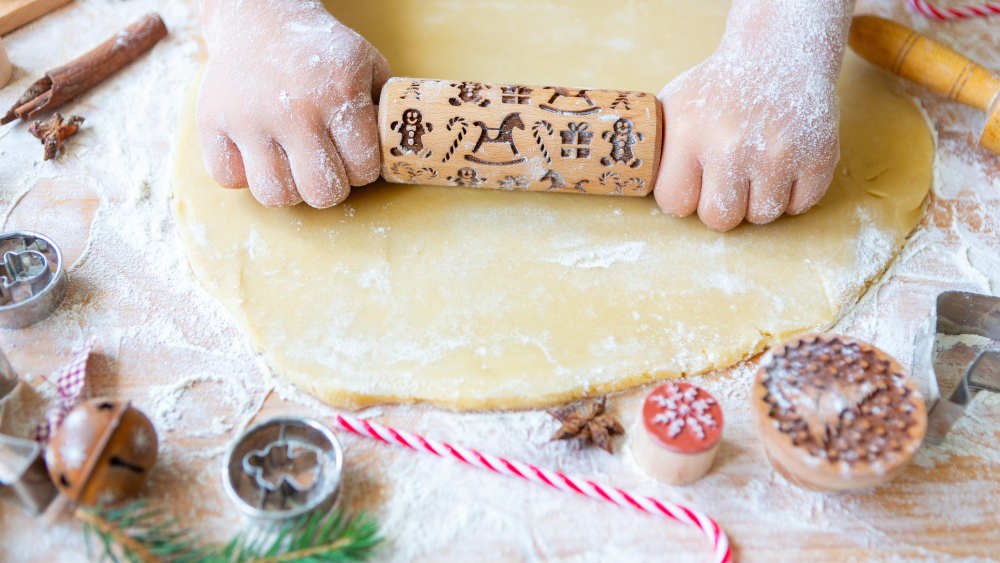 Hände, die einen Teig ausrollen für Weihnachtsplätzchen