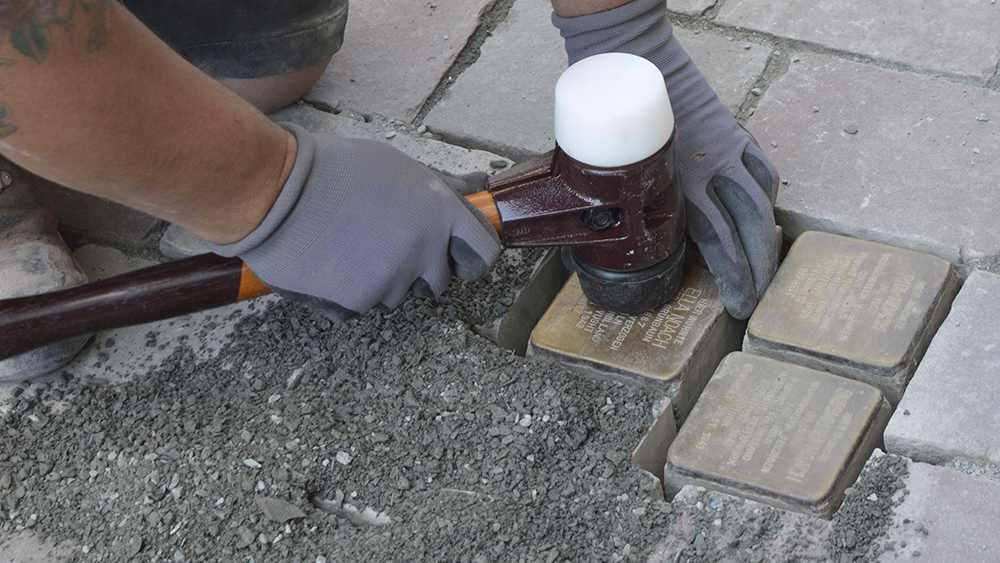 Ein Stolperstein wird mit einem Gummihammer festgeklopft.