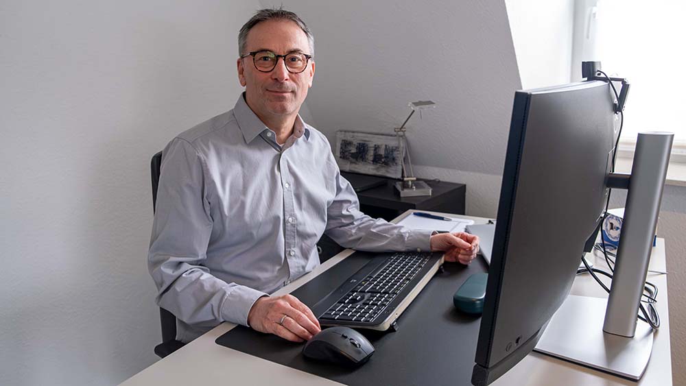 Mann im grauen Hemd sitzt an einem Computer