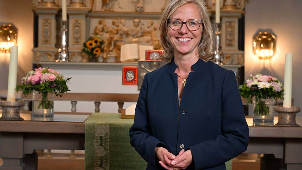 Frau mit blonden Haaren und blauer Bluse steht vor einem Altar