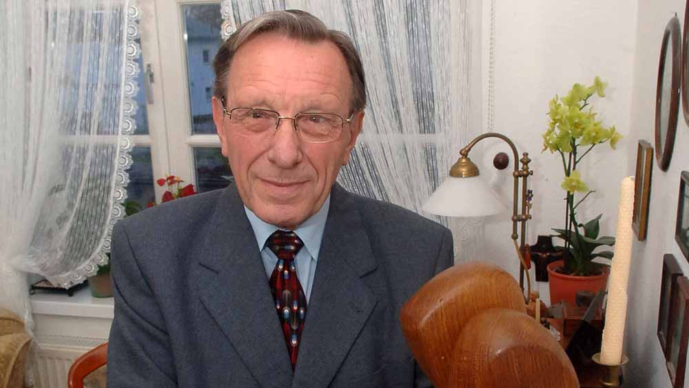 Mann mit Brille und Anzug steht in einem Wohnzimmer