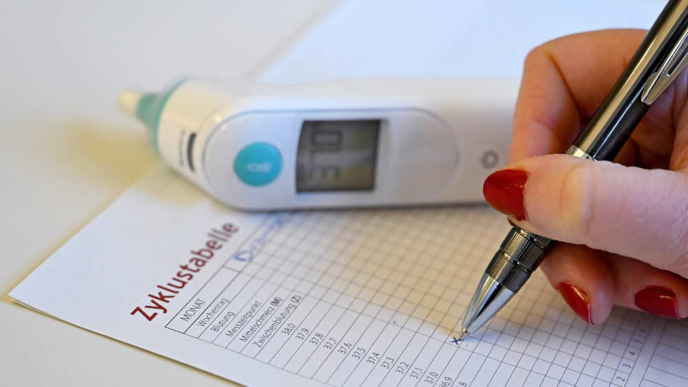 Eine Frau trägt ihre Körpertemperatur in eine Zyklustabelle ein