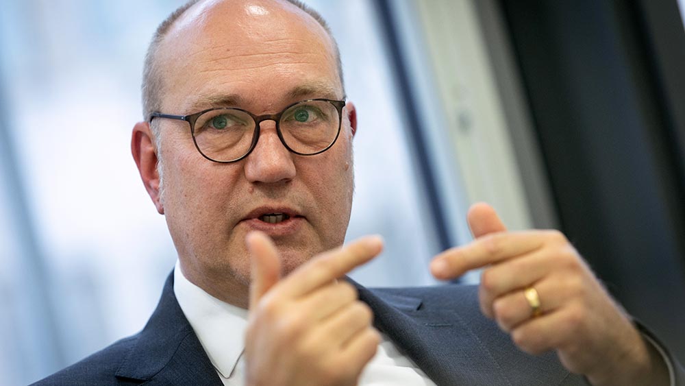 Mann mit Glatze und Brille sitzt an einem Tisch und macht Geste mit Händen