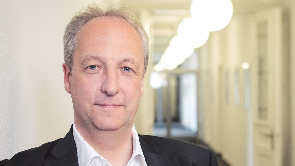 Weißer Mann mit grauen Haaren in einem Büroflur.