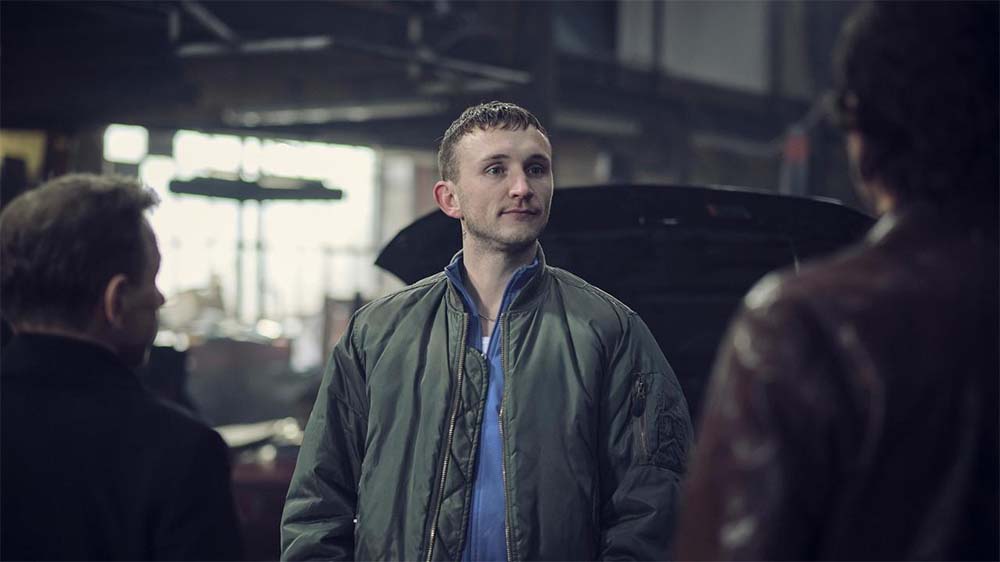 Junger Mann in Bomberjacke steht vor zwei Polizisten