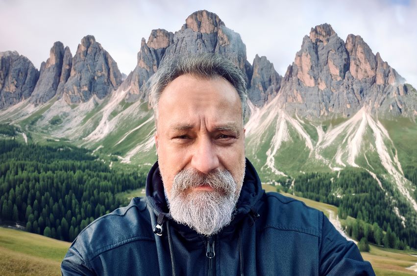 Mann mit grauem Bart vor einem Bergmassiv