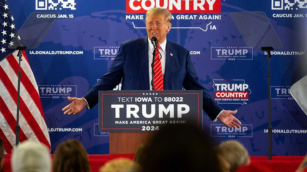 Mann mit blondem Haar im Anzug hält auf Podium eine Rede