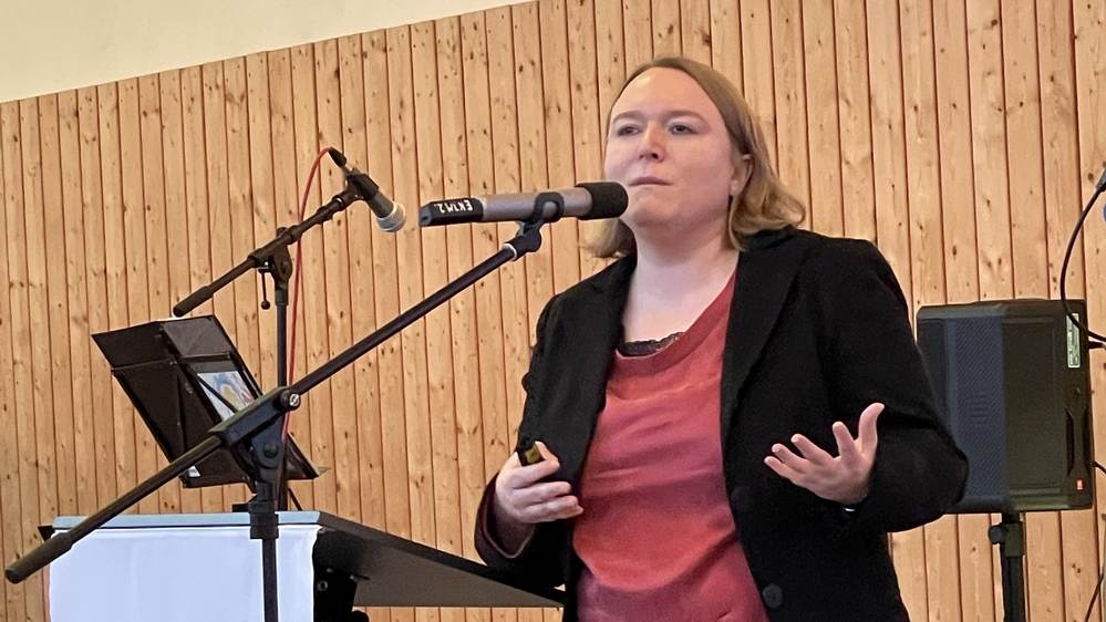 Blonde Frau steht am Mikrofon und erzählt