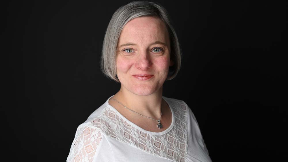 Frau mit grauen, kürzeren Haaren und einer weißen Bluse