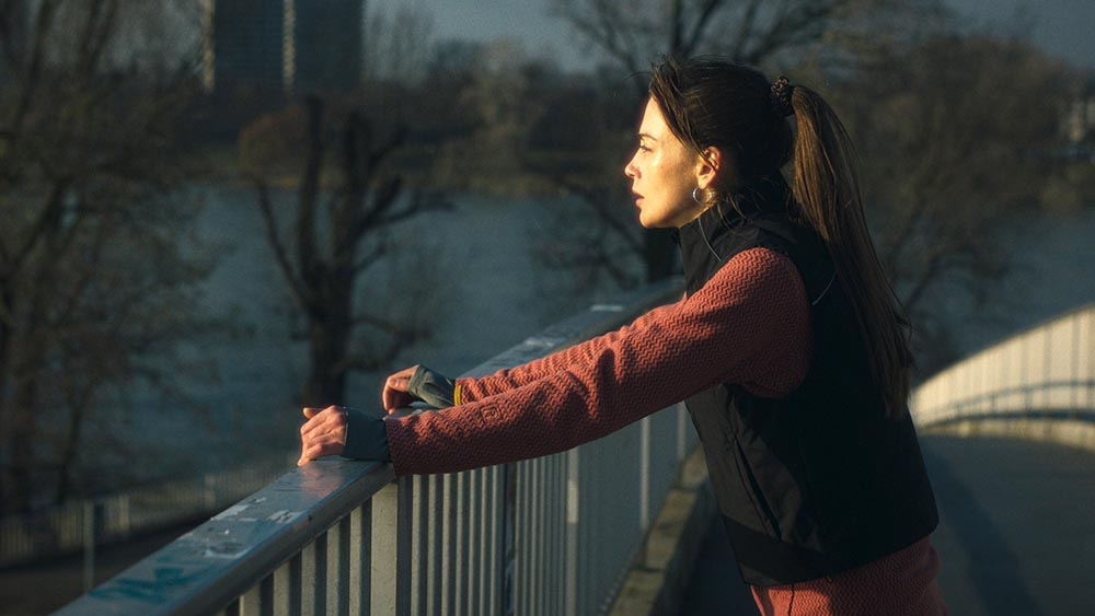 Frau steht in Sportkleidung auf einer Brücke und schaut aufs Wasser