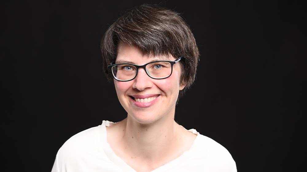 Mittelalte Frau mit dunklen, kurzen Haaren und Brille in weißer Bluse