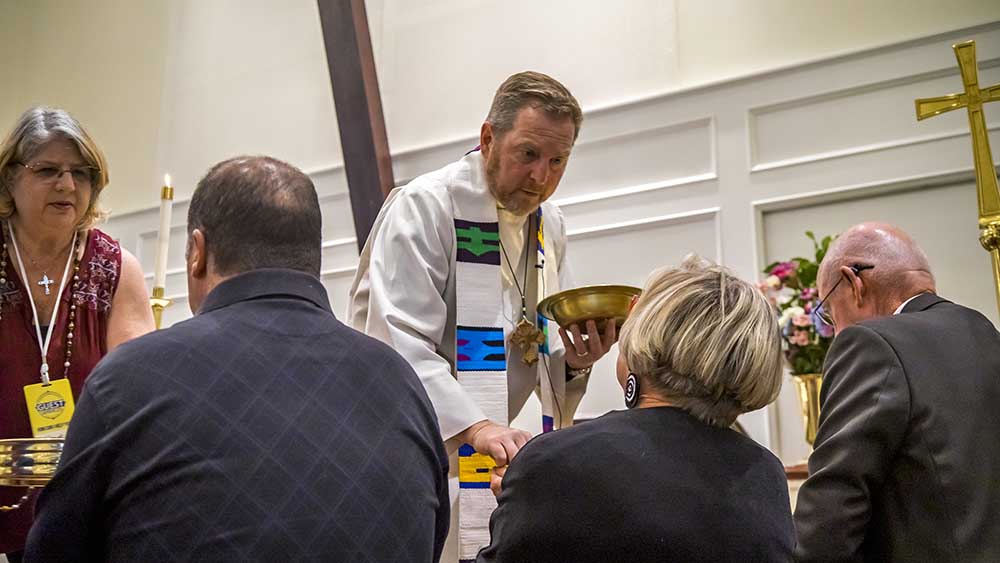 Mann im weißen Talar gibt Menschen auf der Kirchenbank Oblaten in die Hand
