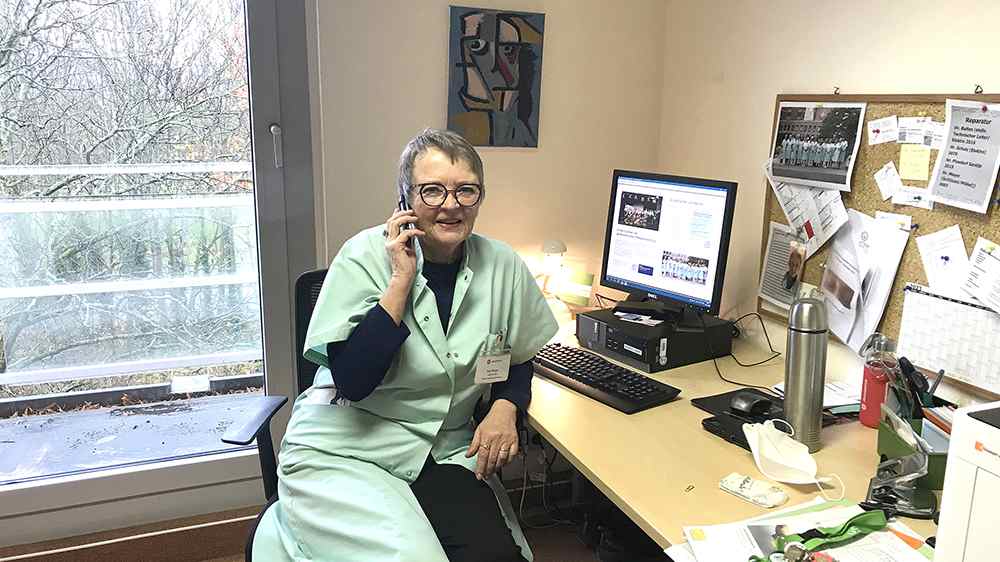 Eine grüne Dame telefoniert im Büro an einem Schreibtisch.