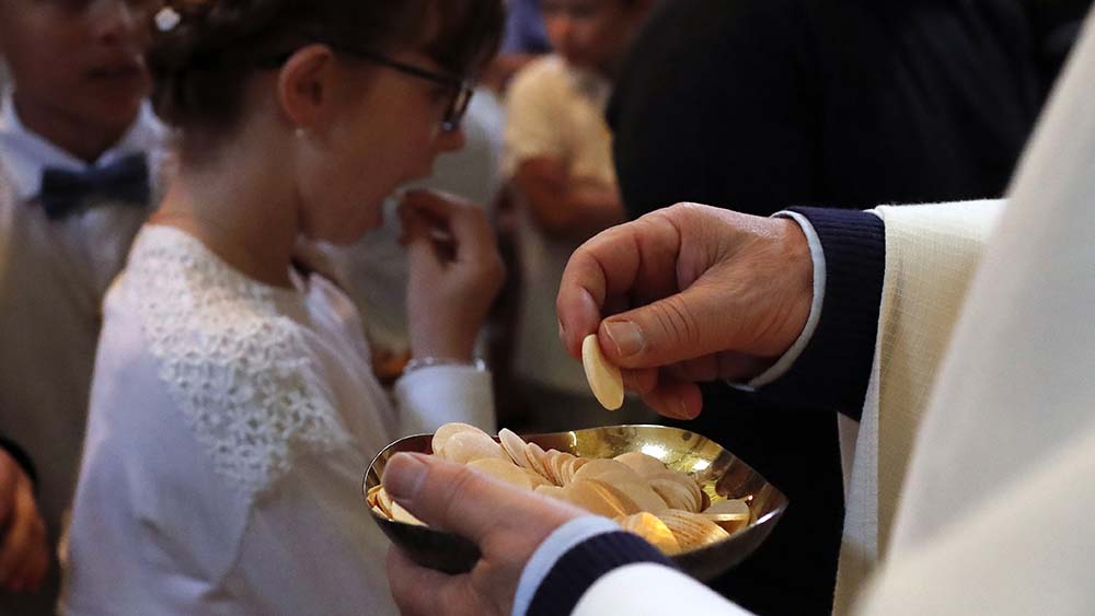 Pfarrer verteilt Hostie an Kinder