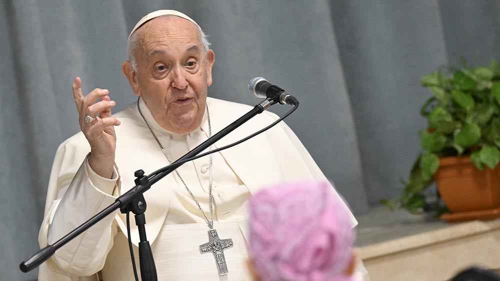 Papst sitzt im weißen Gewand auf einem Stuhl und spricht in ein Mikrofon