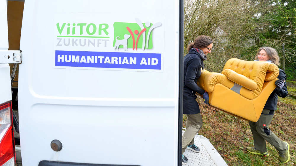 Zwei Frauen laden einen gelben Sessel in einen Transporter