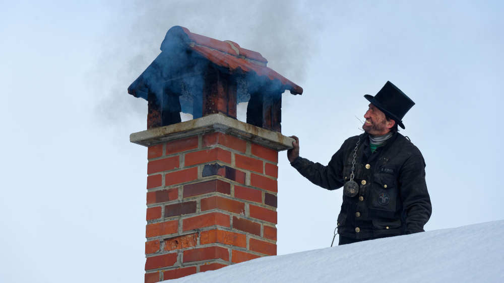 Schornsteinfeger im Winter auf einem Dach mit qualmendem Kamin
