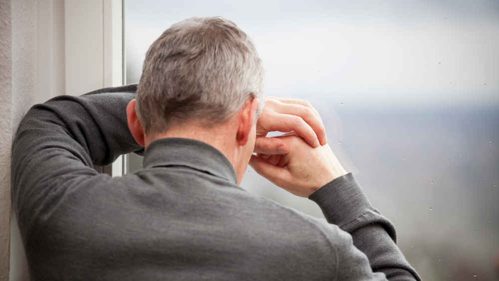 Älterer Mann lehnt sich ans Fenster